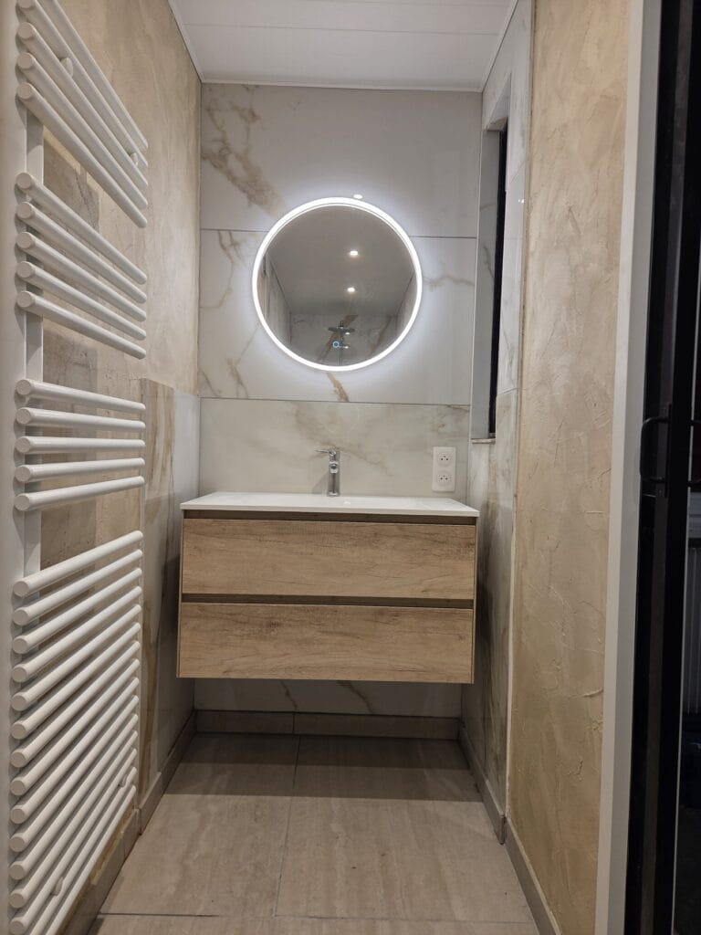 Salle d’eau effet marbre à Battenheim avec meuble vasque bois suspendu, miroir rond LED et sèche-serviettes